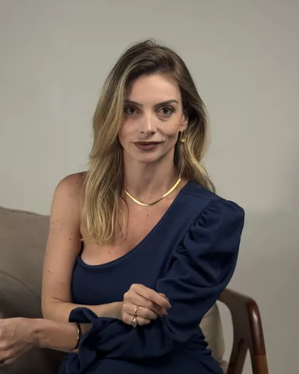 Dra. Débora Giron Galindo sentada numa poltrona, de roupa azul-marinho, sobre fundo claro